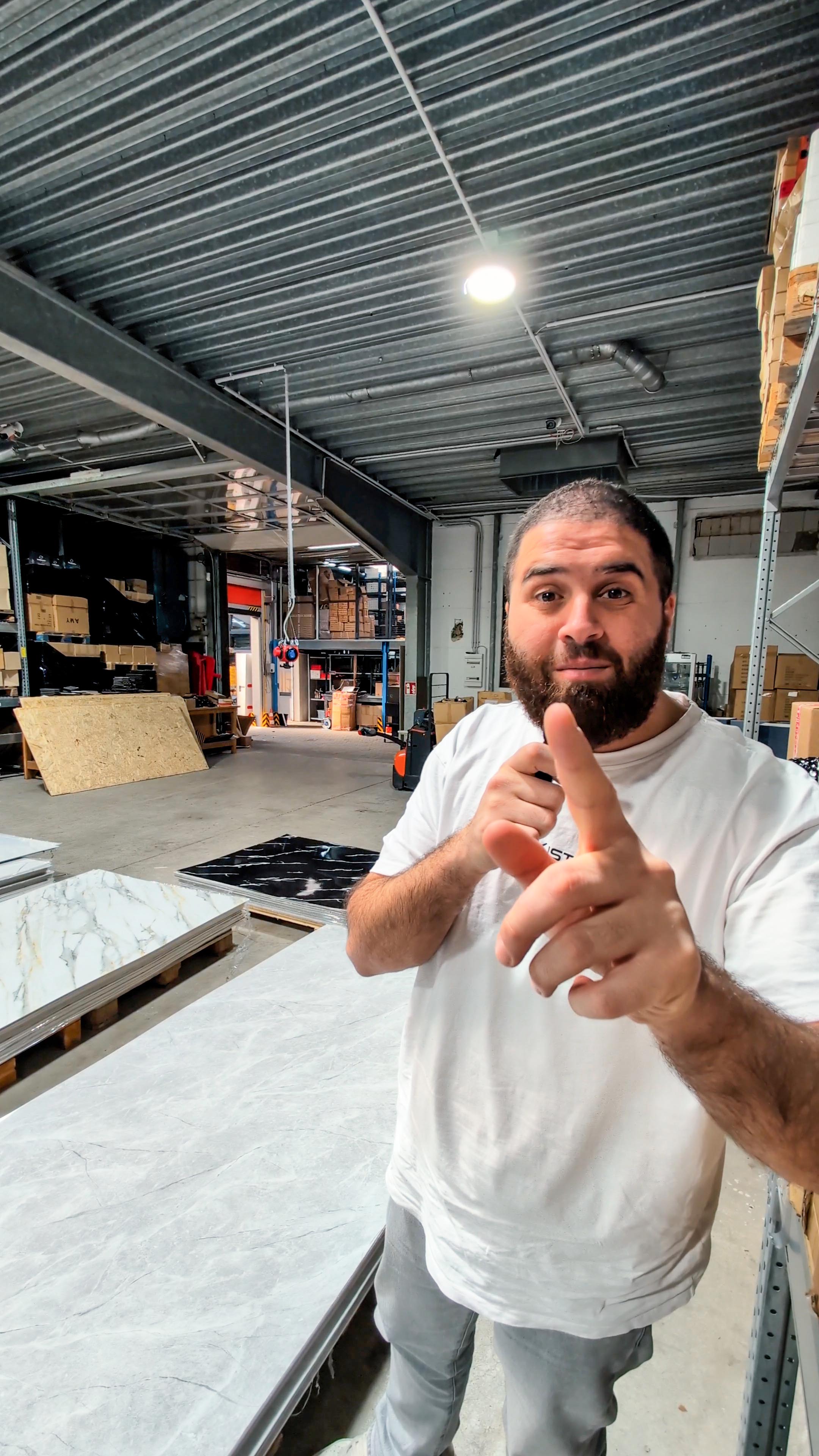 Mann zeigt auf PVC Wandpaneele in Marmor-Optik weiß im AKUSTIL Lager – moderne Wandverkleidung